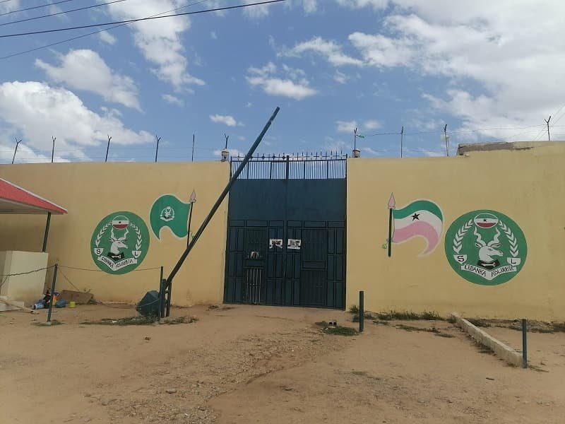The steel gate of a walled facility, national crests painted either side