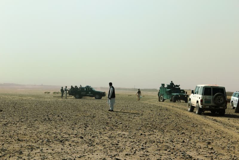 Vehicles halted on open stony ground under a pale sky
